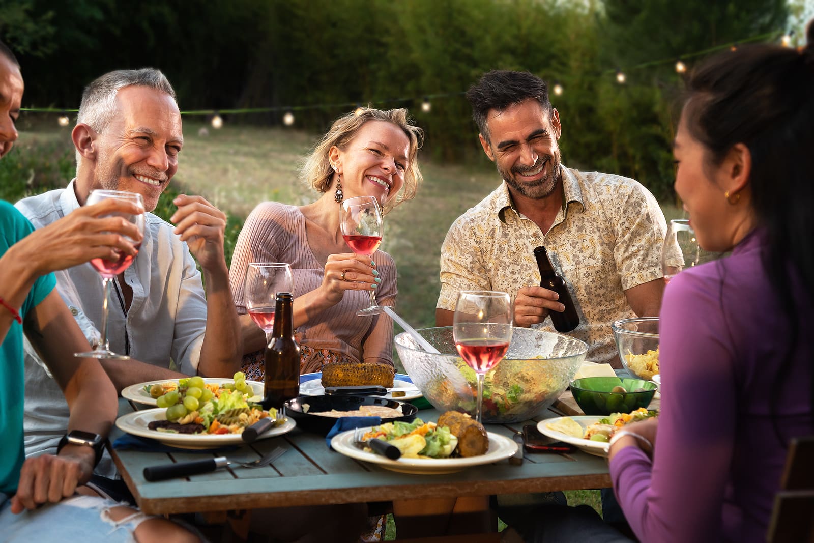 Friends laughing, talking and drinking wine at garden dinner party in the evening.